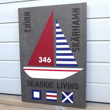 New England inspirerad tavla med segelbåt och signalflaggor samt texterna TJÖRN, SKÄRHAMN, SEASIDE LIVING